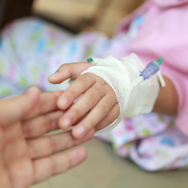 A kid's hand with saline IV solution reaches for an adult's hand — first opinion coverage from STAT